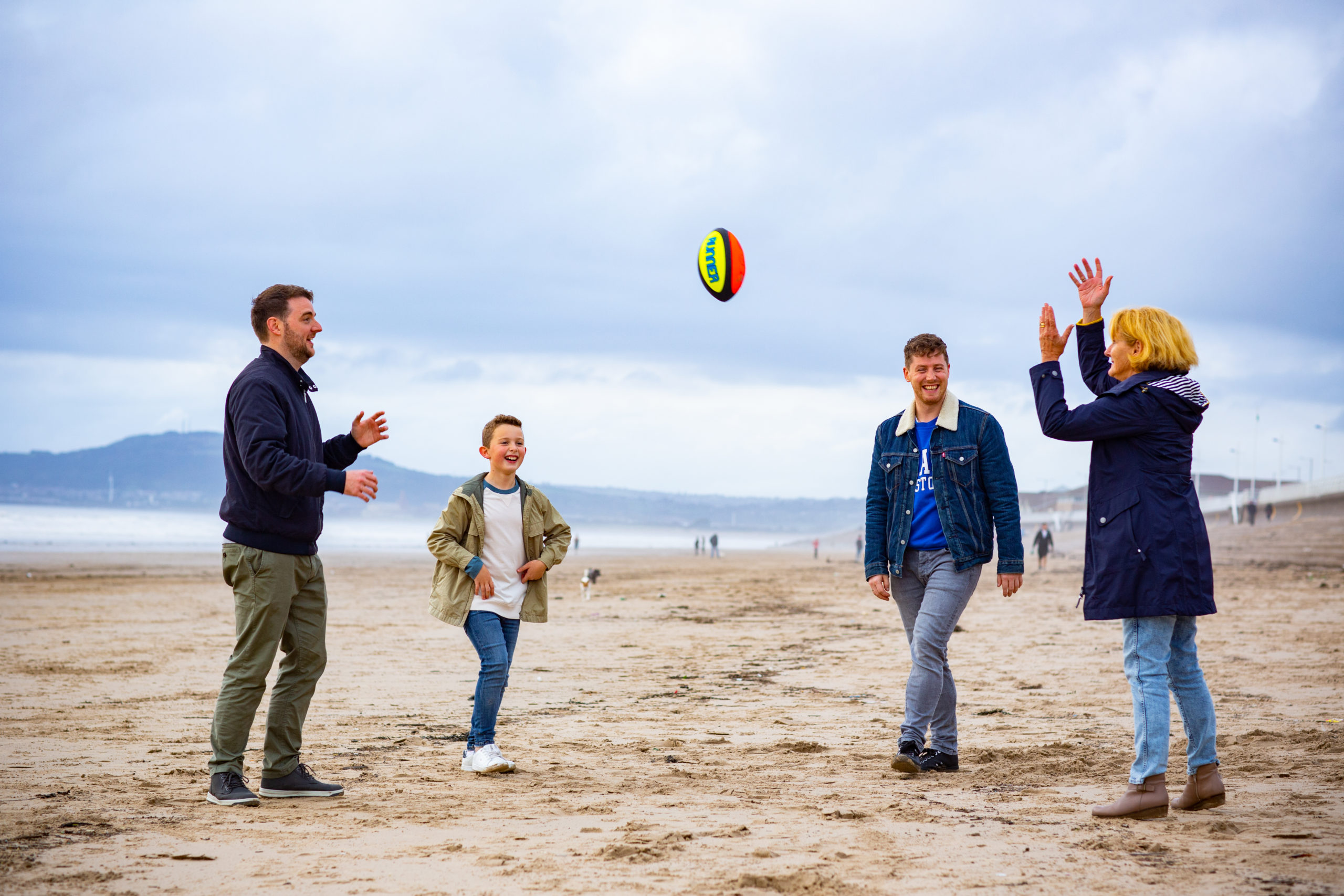a woman, man, teenage boy and young boy playing catch on the beach